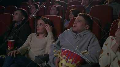 Young guy scared while watching horror film in movie theatre