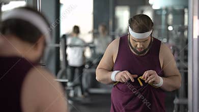 Man measuring fat waist, dissatisfied with his result after dieting and training