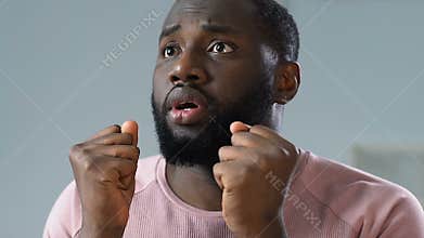 Worried black man watching game on TV, praying for victory and celebrating goal