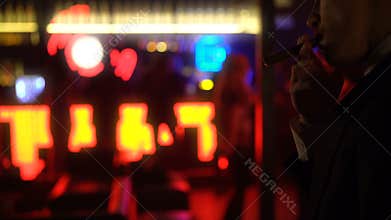 Businessman smoking cigar in elite bar, night club atmosphere, women dancing