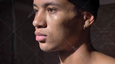Young african-american serious man with hairband looking sideways, guy with pierced ear