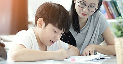 Asian mother with son doing homework in living room.