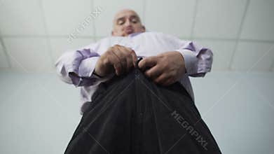Bottom view of corpulent male zipping his pants with great effort, overweight