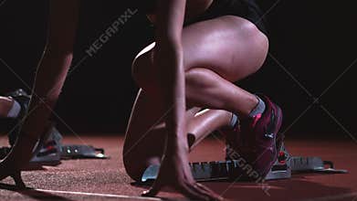 Female runners at athletics track crouching at the starting blocks before a race. In slow motion.