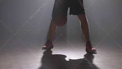 Close footage of basketball player`s legs playing with ball in dark misty room with smoke