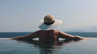 Woman with straw hat relaxing in infinity swimming pool with sea view at luxury resort. summer vacation