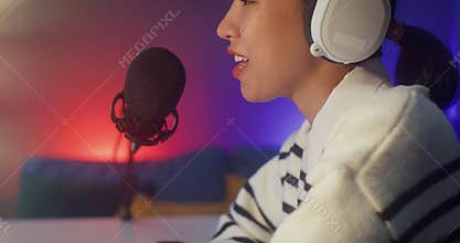 Happy asia lady blogger music influencer record a podcast on computer with headphones and microphone talk with audience in living