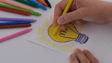 Woman colouring a drawing of Light Bulb with yellow wax crayon.