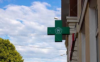 The green cross logo. Pharmacy, sign on the street on the facade of the building against the sky