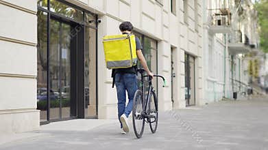 Delivery man walking with bike and yellow bag, rear view