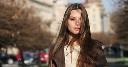 Attractive young lady is walking on the alley full of trees, looks into camera and mesmerizing with her incredible look