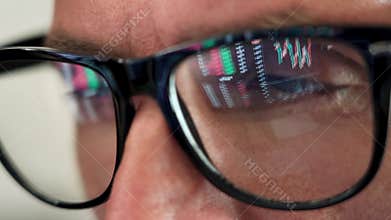Trader looking at computer screen analyzing trading chart reflecting in glasses.
