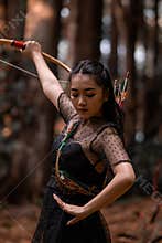 Portrait shot of Indonesian women wearing black dresses with black long hair aiming a bow and an arrow to the sky
