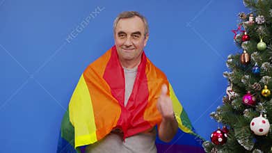 Senior gay man smiling in front of camera with rainbow flag at background. Concept of pride.