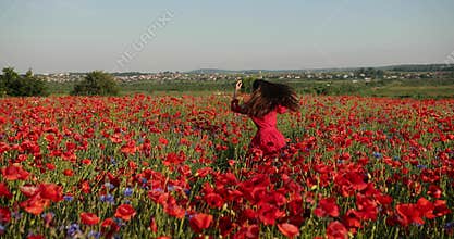 Incredible brunette woman circling and having fun through a poppy field. Charming lady in a red polka dot dress with