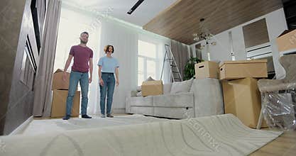 Young caucasian couple spreads a carpet in living room in a new apartment. Couple putting mat when moving in new in