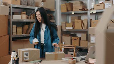 Waist up portrait view of the brunette asian woman scanning parcels while working at the warehouse alone. Shelves with