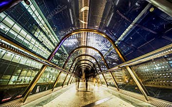 Workers hurry back home through a glass protected gateway between office buildings at night
