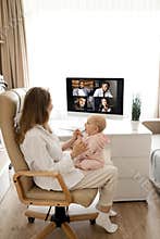 Young woman working at desk at home with computer holding crying tired infant baby holding business meeting at home