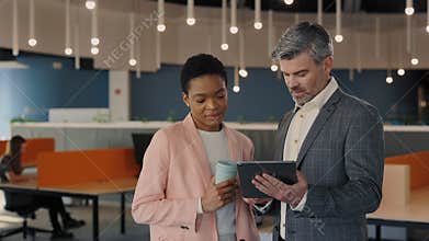 Two diverse people in stylish wear standing together at business center and discussing common project. Colleagues