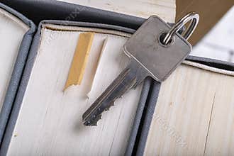 The key to the door in a single-family house laid on the spines of books. Metal key for patent lock