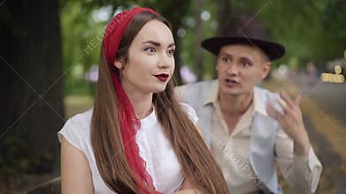 Portrait of irritated young beautiful woman listening to blurred man arguing with her at the background. Annoyed bored