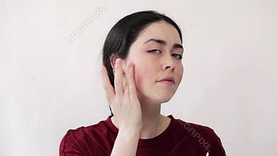 Portrait of a young woman squeezing cream out of a tube, and masking redness on her cheeks with cosmetics. White background. The c