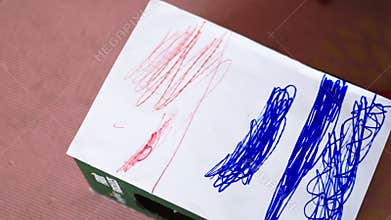 Little girl intensely coloring a white paper box with a red pencil