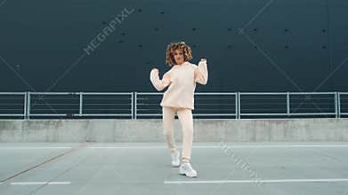 Fashionable funky curly afro dancer woman in sportswear is performing outdoor street dancing motion. Joyful summer