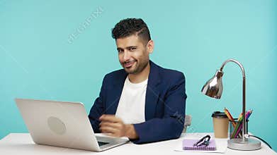 Handsome playful businessman saying come here calling with finger and looking at camera with smile, working on laptop in office