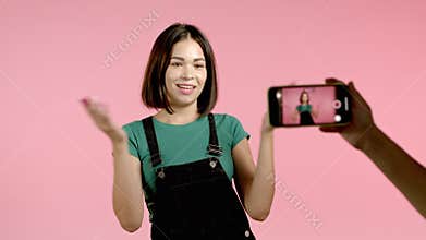 Smiling fashion blogger woman making online new video blog, vlog, with her smartphone on pink background. Influencer