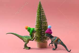 cute dinosaurs wearing knitted hats near christmas tree on a soft pink background