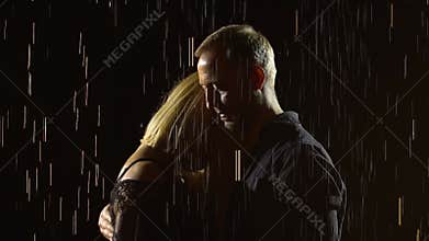 A cute young couple hugging in the rain and enjoying the moment. Close up man and woman on a black studio background