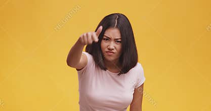 Angry asian woman pointing finger to camera, suspecting and blaming in lying, orange background