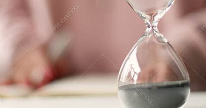 Businesswoman or freelancer worker plans his work schedule in a notebook. Hourglass on table office with copy space