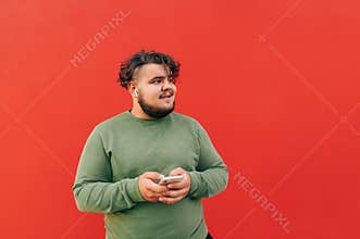 Satisfied attractive young hispanic man is using wireless earphones to listen to the music on his mobile phone, enjoying the