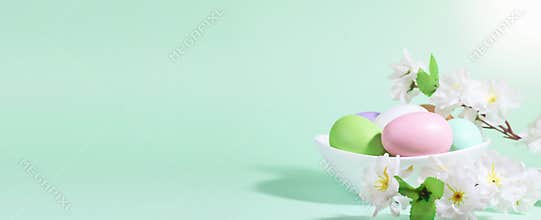 Easter eggs, pink, green and lilac, in a white plate, next to flowers on a green blue background, in the rays of the sun. Pastel
