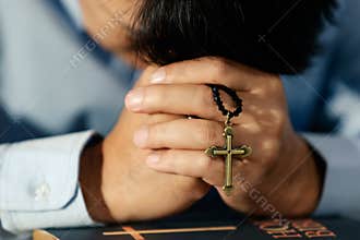 Asian man bowing his head on the Bible and carrying a cross. According to the beliefs of Christianity Is the salvation of Jesus.