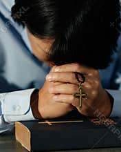 Asian man bowing his head on the Bible and carrying a cross. According to the beliefs of Christianity Is the salvation of Jesus.
