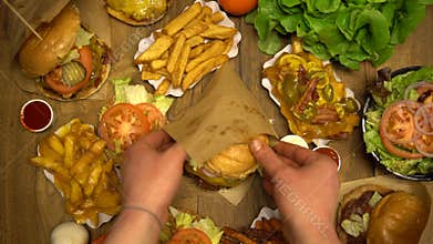 Serving burger in a paper wrap on a table full of fast food dishes. Top down overhead view of unhealthy fried meals on a