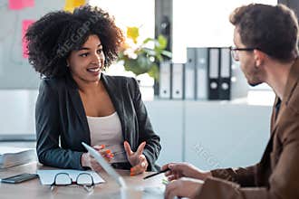 Two smart multiethnic business people working together with laptop while talking about job news in the office