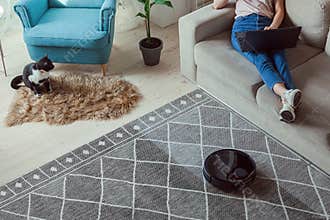 Robot vacuum cleaner cleaning carpet, woman using laptop sitting