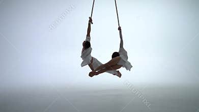 Aerial straps duo wearing white costume on white background doing performance