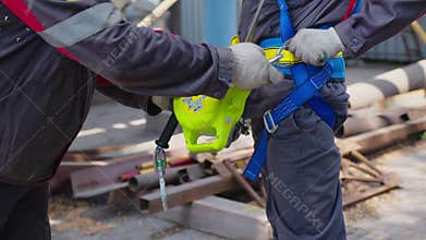 Industrial climber puts on equipment for high-altitude work. On climber s belt carabiners.