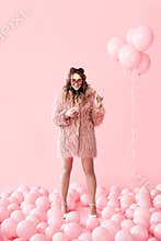 Full length portrait of glamour young woman typing on mobile smartphone over pink balloons background