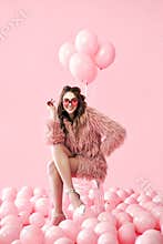 Confident fashion woman sitting on chair posing on many pink balloons background