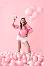 Full length portrait of happy dancing woman with milk shake over pink balloons background.