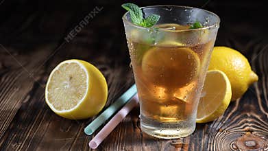 Glass of iced tea with ice cubes and sliced lemon, fresh mint on rustic wooden background. Healthy refreshing lemonade