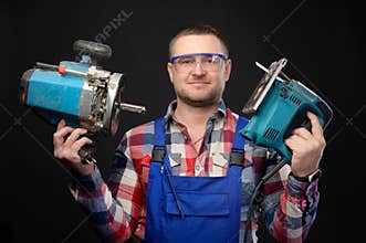 Caucasian repairman in goggles holding woodworking tools. Carpenter portrait on black studio background