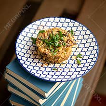 Rice with vegetables and green onions. Plate of pilaf on Stack or tower of books. Blurred background